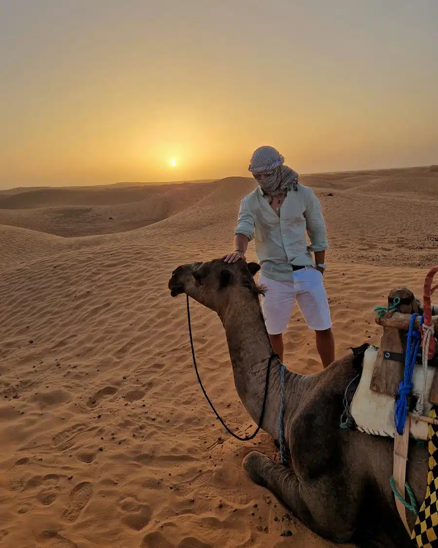 Gabriel junto a un camello al atardecer en las dunas del Sáhara